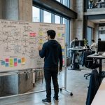 Ingeniero de software revisando diagramas de arquitectura y flujos de APIs en una pizarra de oficina de empresa tecnológica con información confidencial expuesta